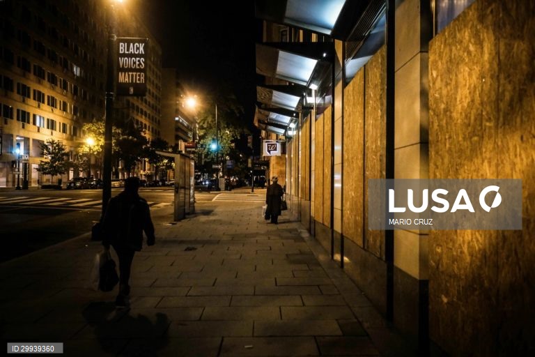 People pass by a store protected with wooden boards in Washington DC, United States, 01 November 2020 (issued on 02 November 2020). Downtown Washington DC meets commercial establishments protected by plywood boards for fear of "disturbances" after the release of the presidential election results and signs of protest from the "Black Lives Matter" movement near the White House railings where a demonstration is being prepared for election night. MARIO CRUZ/LUSA