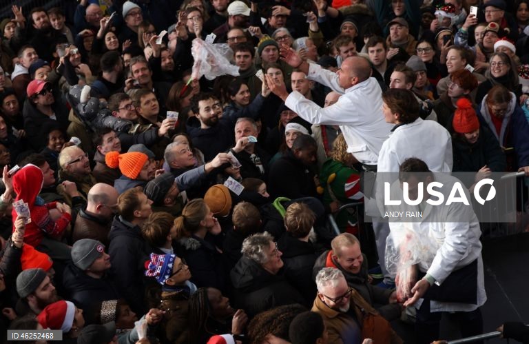 Pessoas observam enquanto talhantes distribuem carne no leilão de carne de Natal em Smithfield, Londres, Grã-Bretanha. Centenas de pessoas reunem-se para ter a oportunidade de comprar carne a preços promocionais na véspera de Natal no mercado de Smithfield, em Londres.