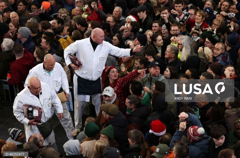 Pessoas observam enquanto talhantes distribuem carne no leilão de carne de Natal em Smithfield, Londres, Grã-Bretanha. Centenas de pessoas reunem-se para ter a oportunidade de comprar carne a preços promocionais na véspera de Natal no mercado de Smithfield, em Londres.