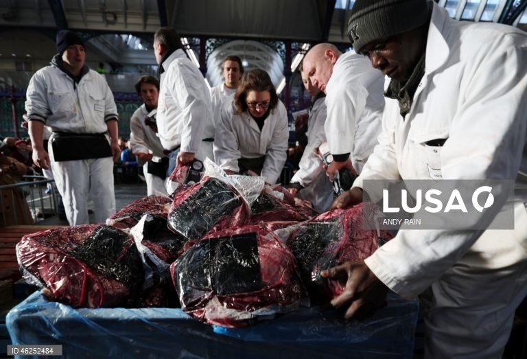 Pessoas observam enquanto talhantes distribuem carne no leilão de carne de Natal em Smithfield, Londres, Grã-Bretanha. Centenas de pessoas reunem-se para ter a oportunidade de comprar carne a preços promocionais na véspera de Natal no mercado de Smithfield, em Londres.