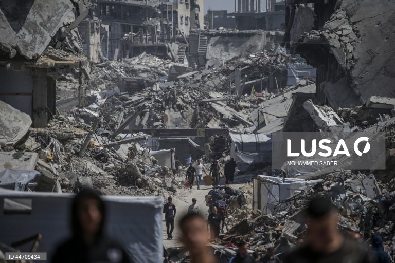Palestinianos deslocados passam pelos escombros de edifícios destruídos no campo de refugiados de Jabalia, no norte da Faixa de Gaza, depois de o exército israelita ter emitido ordens de evacuação para as zonas do norte e do leste da Faixa de Gaza.